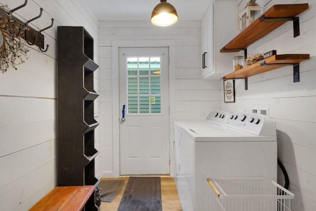 laundry area featuring wood walls, washer and clothes dryer, cabinets, and light hardwood / wood-style floors