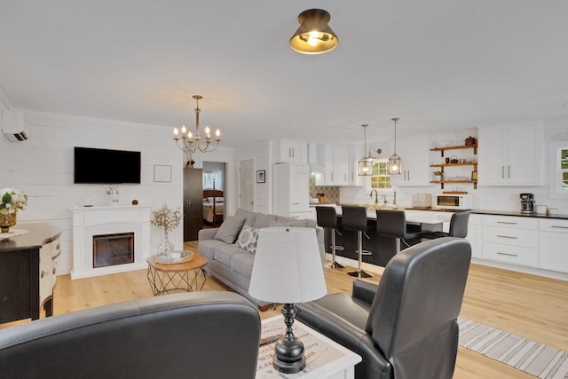 living room with sink, a chandelier, a wall mounted air conditioner, and light wood-type flooring