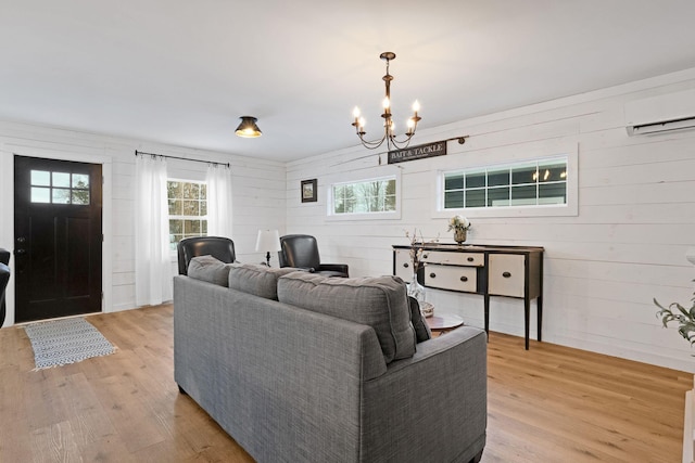 living room featuring wooden walls, light hardwood / wood-style flooring, a notable chandelier, and a wall unit AC