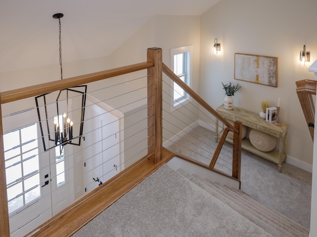 stairs with carpet flooring, a healthy amount of sunlight, vaulted ceiling, and a notable chandelier