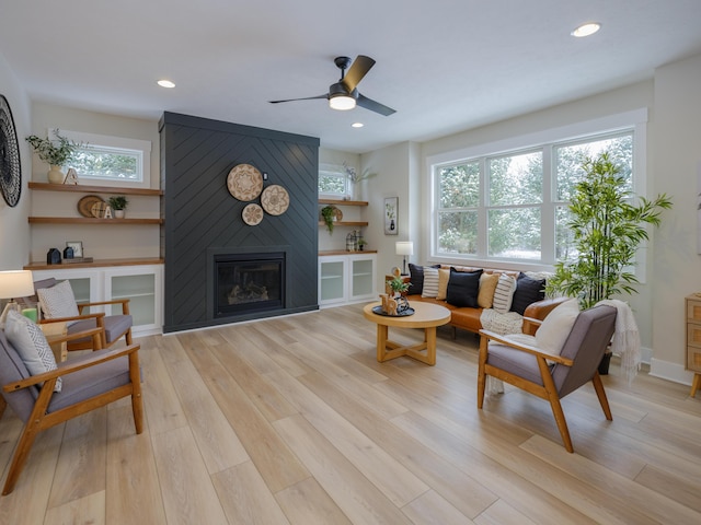 living room with ceiling fan, a large fireplace, and light hardwood / wood-style flooring