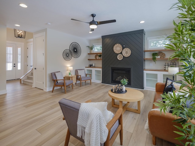 living room featuring a fireplace, ceiling fan with notable chandelier, and light hardwood / wood-style flooring