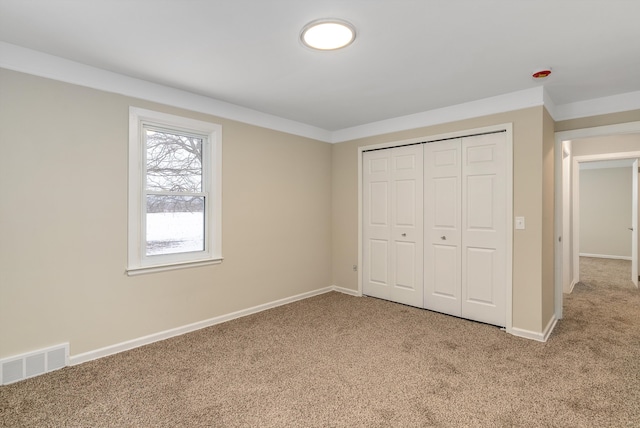 unfurnished bedroom featuring carpet flooring, crown molding, and a closet