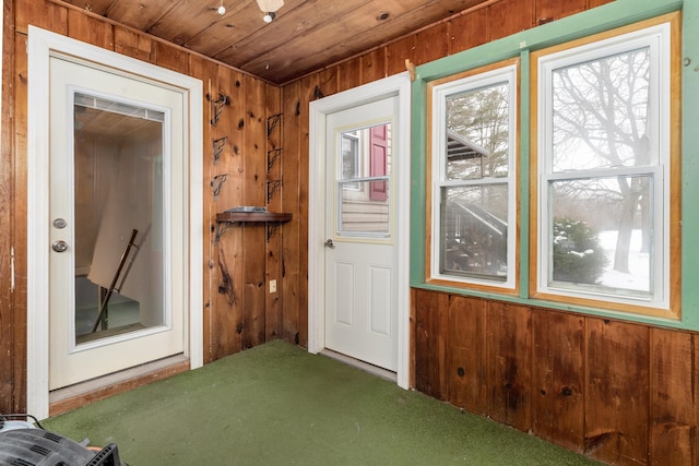 doorway to outside with carpet, wood walls, and wooden ceiling