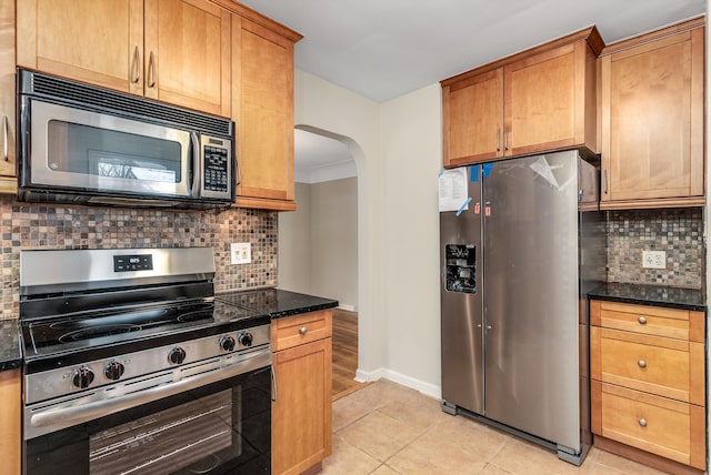 kitchen with tasteful backsplash, light tile patterned floors, appliances with stainless steel finishes, and dark stone counters