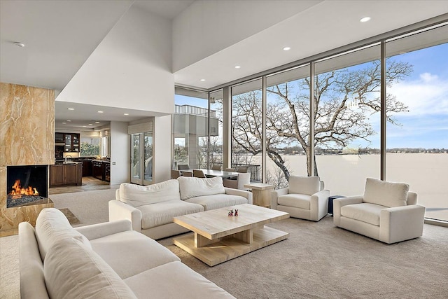 living room featuring a towering ceiling, a wall of windows, a water view, and a fireplace