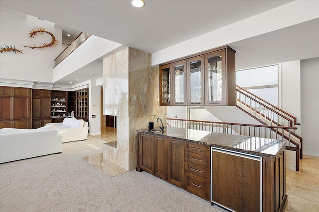 bar with light carpet, dark brown cabinetry, dark stone counters, and sink