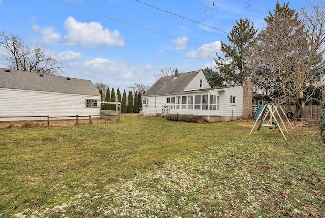 rear view of property featuring a sunroom, a playground, and a yard