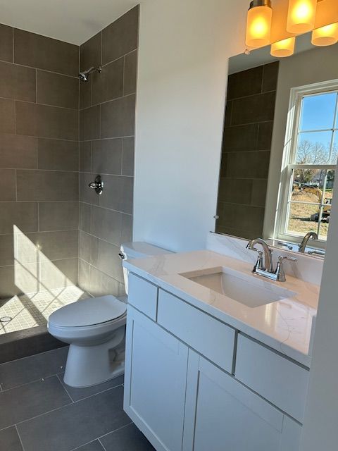 bathroom with tile patterned flooring, a tile shower, vanity, and toilet