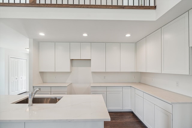 kitchen with dark hardwood / wood-style flooring, white cabinetry, sink, and light stone counters