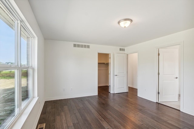 unfurnished bedroom with a closet, a spacious closet, multiple windows, and dark hardwood / wood-style floors