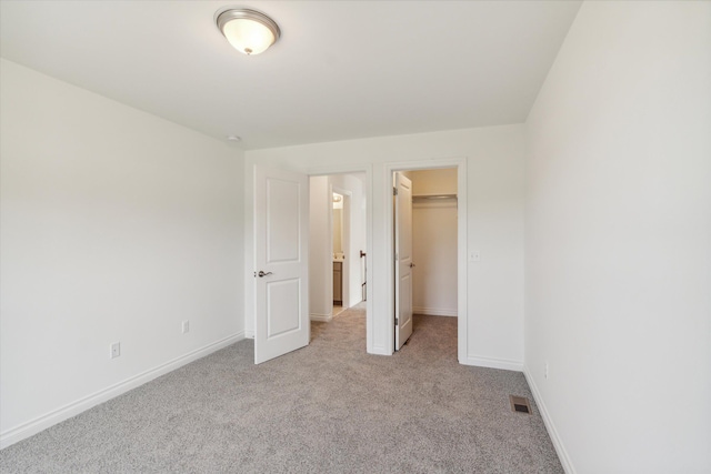 unfurnished bedroom featuring a walk in closet, light carpet, and a closet