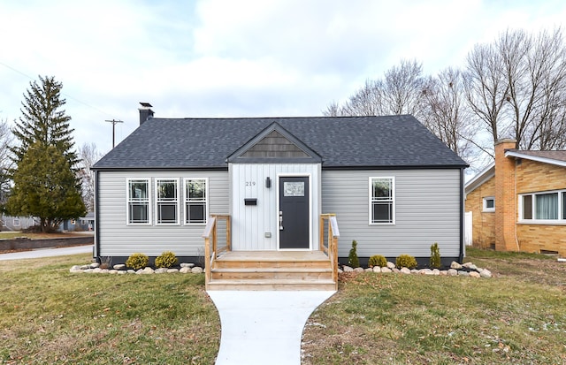 view of front of home featuring entry steps, a shingled roof, a chimney, board and batten siding, and a front yard