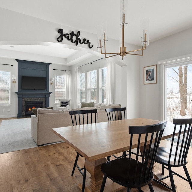 dining area with a large fireplace, light wood-type flooring, and a notable chandelier