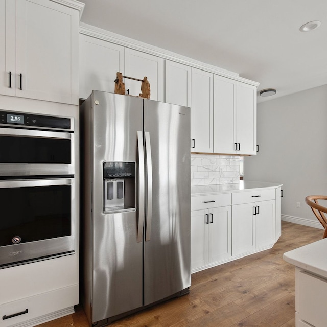 kitchen with appliances with stainless steel finishes, light hardwood / wood-style flooring, white cabinetry, and tasteful backsplash