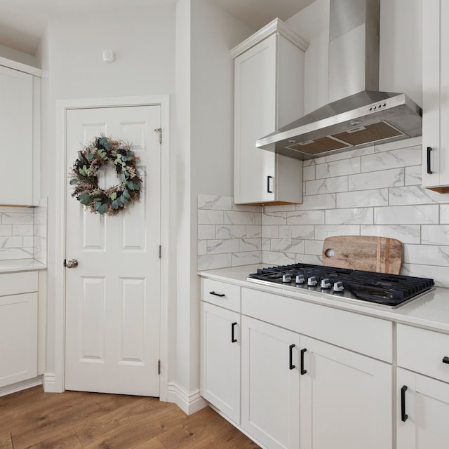 kitchen with white cabinets, wall chimney range hood, light hardwood / wood-style floors, and tasteful backsplash