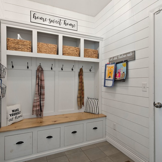 mudroom with dark tile patterned floors and wooden walls