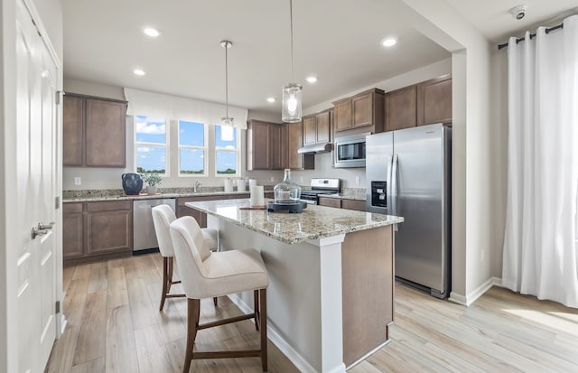 kitchen featuring a kitchen island, appliances with stainless steel finishes, a kitchen breakfast bar, hanging light fixtures, and light wood-type flooring