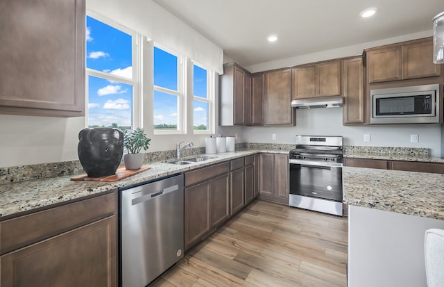 kitchen with light stone counters, sink, stainless steel appliances, and light hardwood / wood-style floors