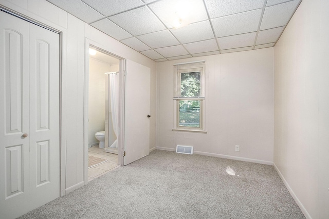 unfurnished bedroom with a paneled ceiling, connected bathroom, and light carpet