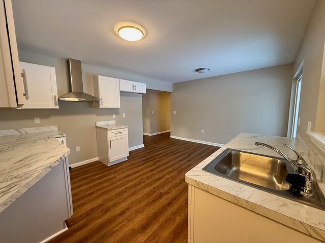 kitchen with white cabinets, wall chimney exhaust hood, sink, and dark wood-type flooring