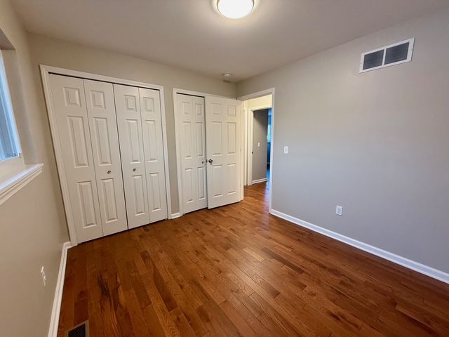 unfurnished bedroom featuring wood-type flooring and two closets