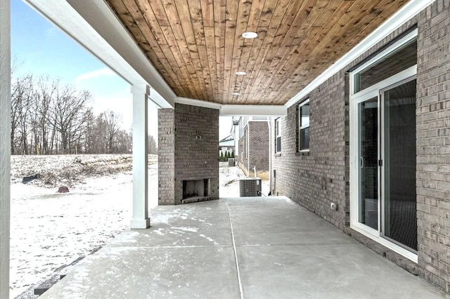 snow covered patio featuring central air condition unit and an outdoor brick fireplace