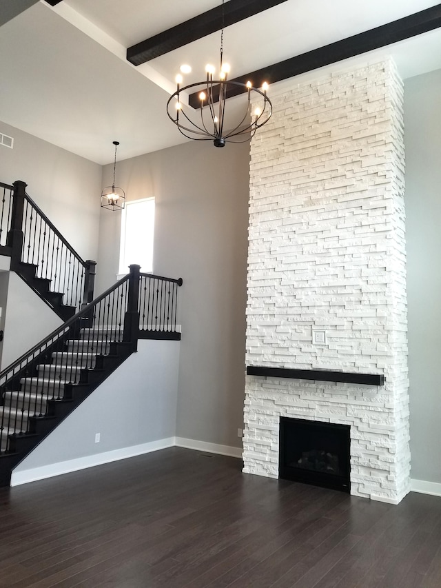 unfurnished living room with beamed ceiling, dark hardwood / wood-style floors, a stone fireplace, and a chandelier