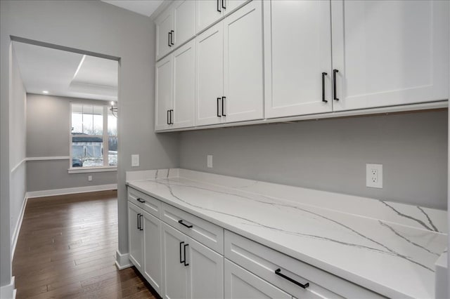 kitchen featuring white cabinets, dark hardwood / wood-style floors, light stone counters, and a tray ceiling