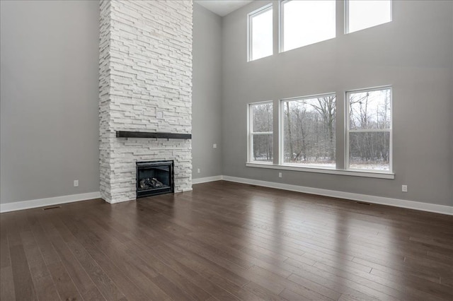 unfurnished living room with a stone fireplace, plenty of natural light, dark wood-type flooring, and a high ceiling