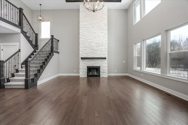 unfurnished living room with a notable chandelier, dark hardwood / wood-style floors, a towering ceiling, and a fireplace