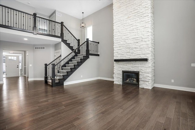 unfurnished living room featuring a fireplace, a towering ceiling, dark wood-type flooring, and a notable chandelier