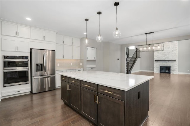 kitchen featuring white cabinets, a stone fireplace, hanging light fixtures, appliances with stainless steel finishes, and dark brown cabinetry