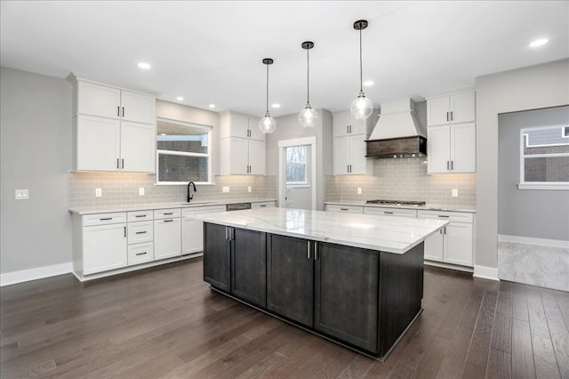 kitchen with white cabinetry, a center island, light stone countertops, hanging light fixtures, and premium range hood