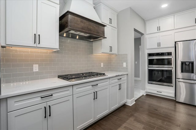 kitchen featuring light stone countertops, appliances with stainless steel finishes, dark hardwood / wood-style flooring, custom exhaust hood, and white cabinetry