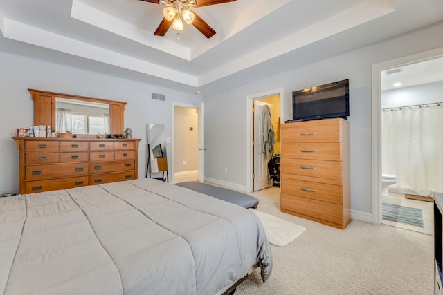 carpeted bedroom with ceiling fan, a tray ceiling, and ensuite bath