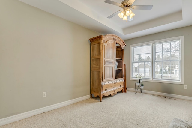 interior space featuring light carpet, a raised ceiling, and ceiling fan