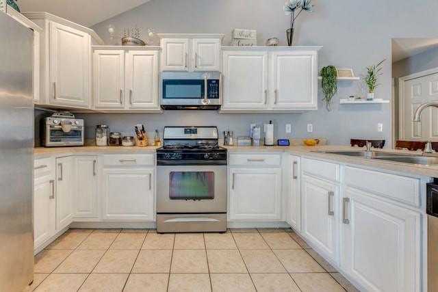 kitchen with white cabinets, sink, vaulted ceiling, light tile patterned floors, and stainless steel appliances