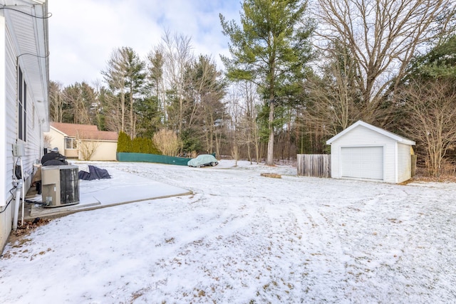 snowy yard featuring a garage, an outdoor structure, and central AC