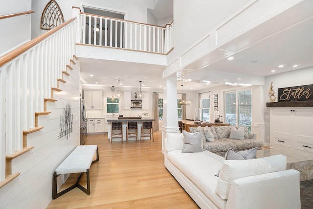 living room with an inviting chandelier, a towering ceiling, and light wood-type flooring