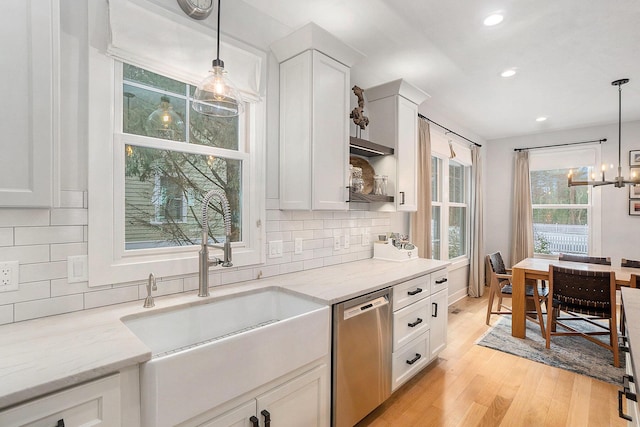 kitchen featuring hanging light fixtures, white cabinetry, stainless steel dishwasher, and light stone counters