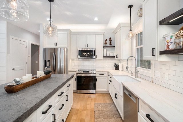 kitchen with sink, light stone counters, pendant lighting, stainless steel appliances, and white cabinets