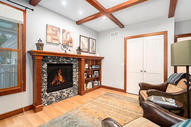 living room with coffered ceiling, wood-type flooring, a stone fireplace, and beam ceiling