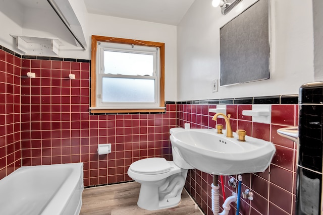 bathroom with a tub to relax in, hardwood / wood-style floors, and tile walls