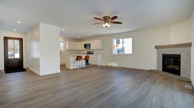 unfurnished living room featuring a stone fireplace, ceiling fan, and light hardwood / wood-style flooring