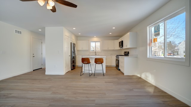 kitchen with white cabinetry, plenty of natural light, a breakfast bar, a kitchen island, and appliances with stainless steel finishes