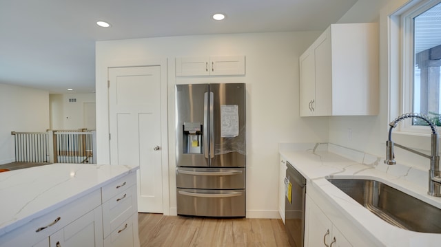 kitchen with sink, light hardwood / wood-style flooring, light stone countertops, appliances with stainless steel finishes, and white cabinetry