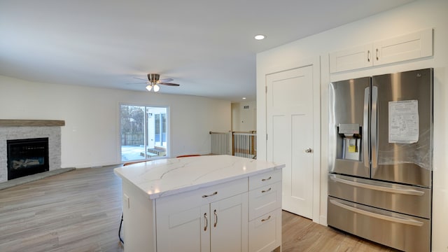 kitchen with a stone fireplace, stainless steel refrigerator with ice dispenser, light stone countertops, a kitchen island, and white cabinetry