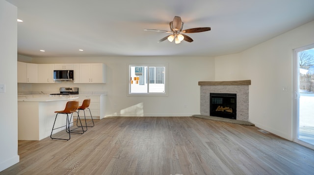 living room featuring ceiling fan, a stone fireplace, and light wood-type flooring