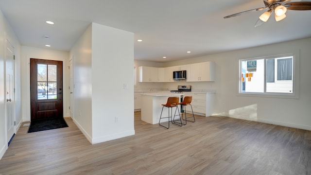 kitchen featuring a kitchen island, stove, a kitchen bar, white cabinets, and light wood-type flooring